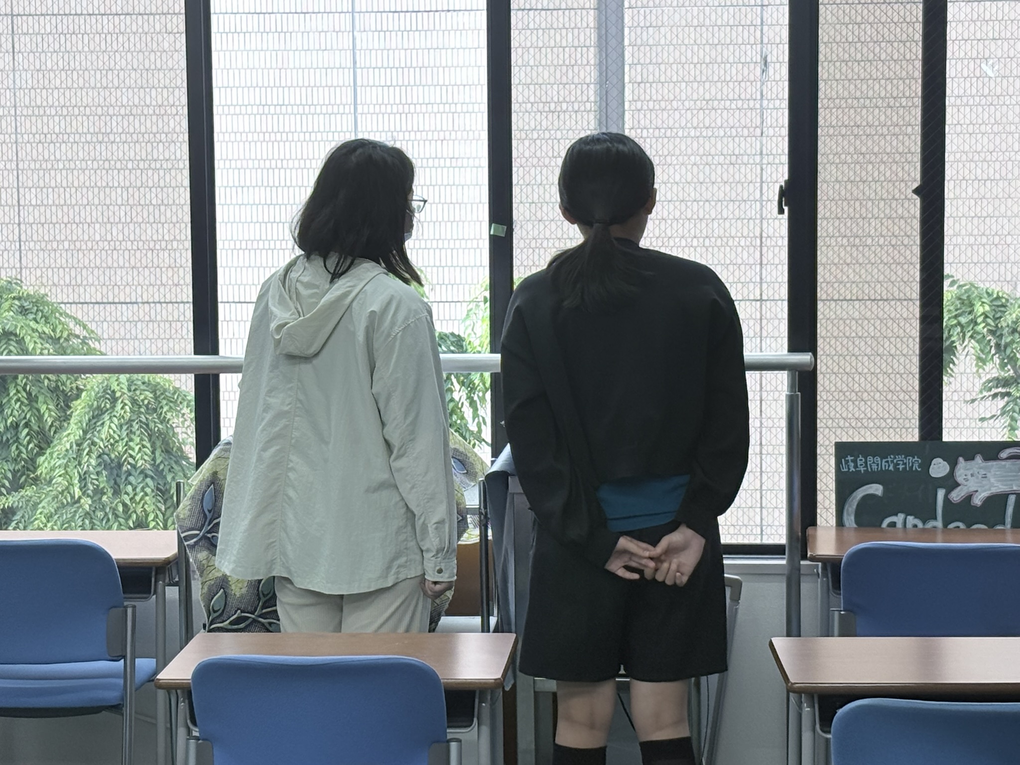 教室の窓辺で話し込む仲良し2人